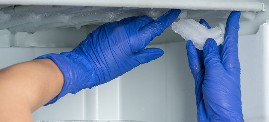 hands in blue gloves removing frost from freezer