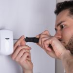 Professional burglar alarm installer fitting a security alarm door sensor on wall