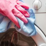 hand in pink glove cleaning washing machine door