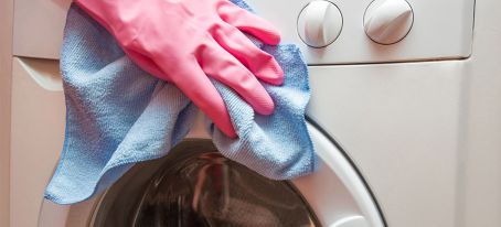 hand in pink glove cleaning washing machine door