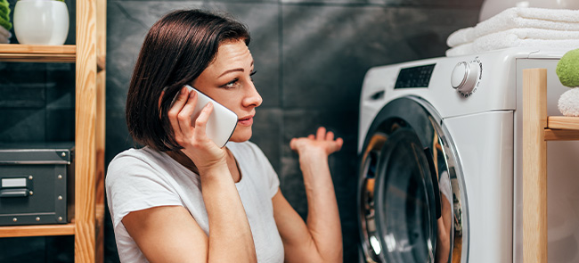 Woman sitting by the washing machine and calling for appliance repair service