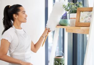 Woman dusting and cleaning objects on a shelf in her living room