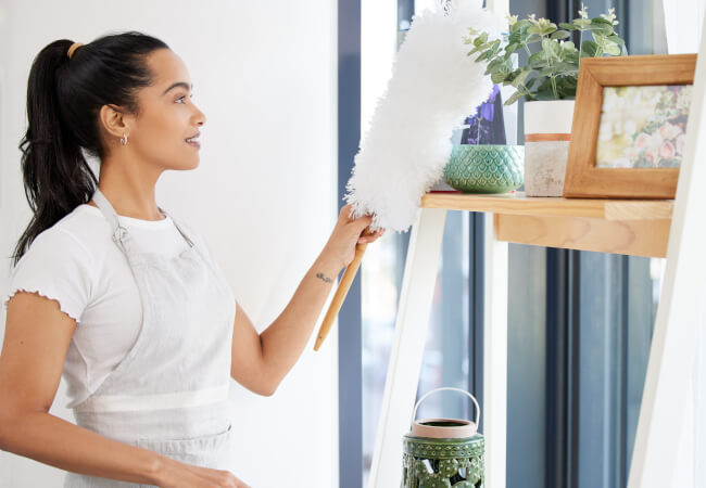 Woman dusting and cleaning objects on a shelf in her living room