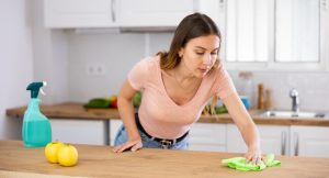 Focused woman wearing casual clothes cleaning stains on countertop in kitchen with a rag and detergent