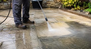 Person pressure washing a stone patio during outdoor cleaning maintenance