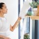 Woman dusting and cleaning objects on a shelf in her living room