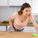 Focused woman wearing casual clothes cleaning stains on countertop in kitchen with a rag and detergent